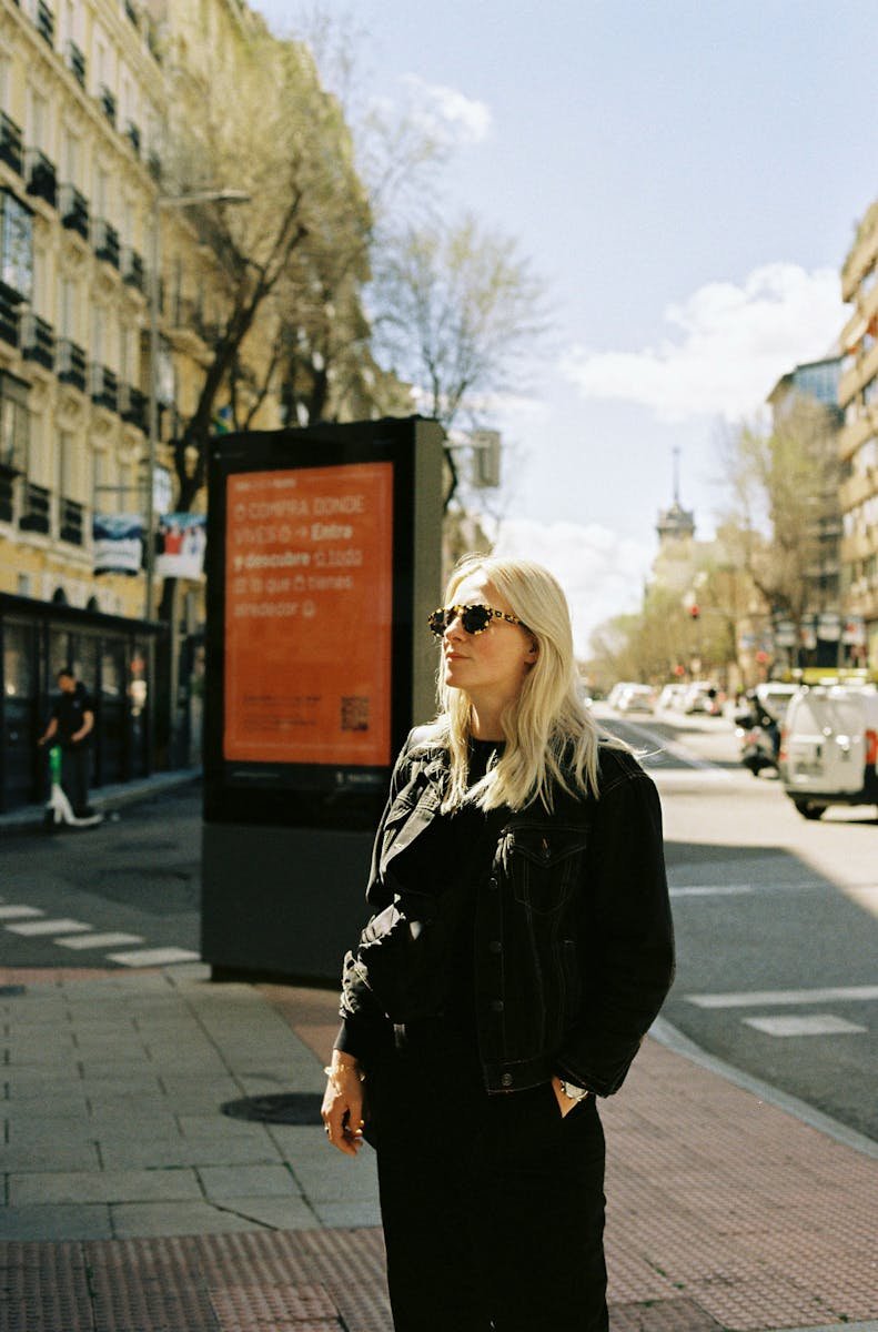 A woman in black jacket and sunglasses standing on a street